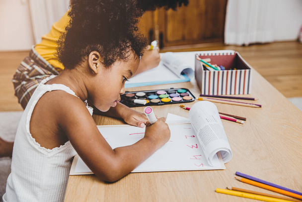 American Black παιδιά προσχολικής ηλικίας που κάνουν τα μαθήματά τους μαθαίνοντας την εκπαίδευση με την αδελφή της που ζουν μαζί στο σπίτι. - Φωτογραφία, εικόνα