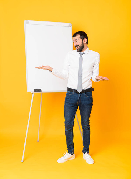 Plan complet de l'homme d'affaires donnant une présentation sur tableau blanc sur fond jaune isolé tenant copyspace avec deux mains
 - Photo, image