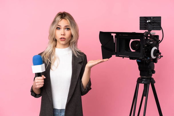 Reporter kobieta trzyma mikrofon i raportuje wiadomości na odosobnionym różowym tle co wątpliwość gest - Zdjęcie, obraz
