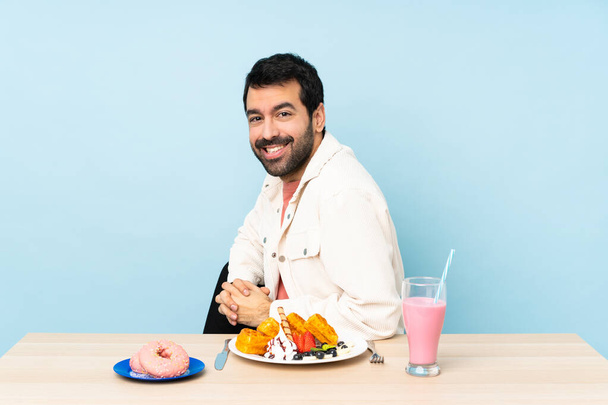 Человек за столом завтракает вафлями и молочным коктейлем со скрещенными руками и смотрит вперед
 - Фото, изображение