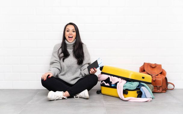 Voyageur fille colombienne avec une valise pleine de vêtements assis sur le sol avec expression faciale surprise - Photo, image