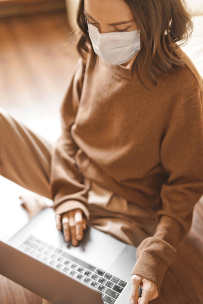 Lifestyle portrait of young lady working at notebook with mask. Woman concept for alternative office freelance. Stay home. Coronavirus. Quarantine. Online training education and freelance work. Coronavirus pandemic in the world - Fotografie, Obrázek