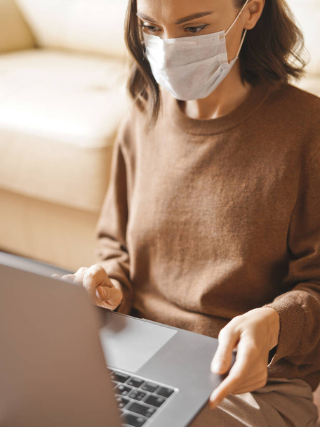 Lifestyle portrait of young lady working at notebook with mask. Woman concept for alternative office freelance. Stay home. Coronavirus. Quarantine. Online training education and freelance work. Coronavirus pandemic in the world - Photo, Image