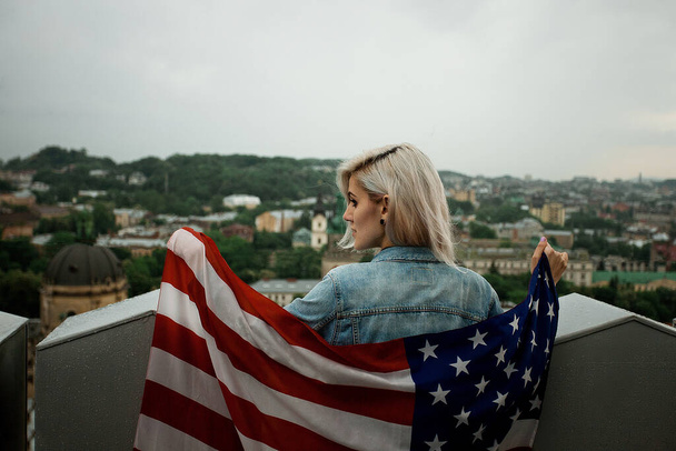 beautiful young blond woman on a city background with american flag - Photo, Image