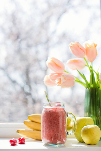 Batido de dieta saludable con fresa, plátano y manzanas en tarro de cristal de albañil. Batido y ramo de tulipanes en alféizar de ventana
 - Foto, imagen