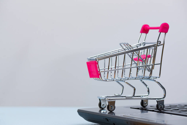 Shopping cart or supermarket trolley with laptop notebook, on grey background and copy space, e-commerce and online shopping concept. - Fotografie, Obrázek