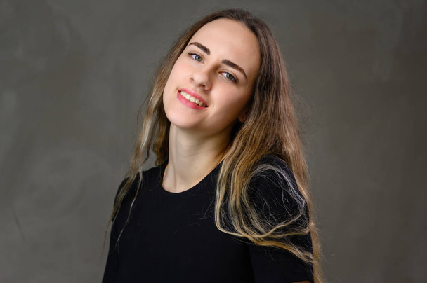 Portrait Caucasian happiness girl in a black dress with long hair and a beautiful smile with straight teeth on a gray background. - Valokuva, kuva
