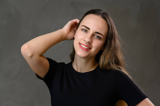 Portrait Caucasian happiness girl in a black dress with long hair and a beautiful smile with straight teeth on a gray background. - Фото, зображення
