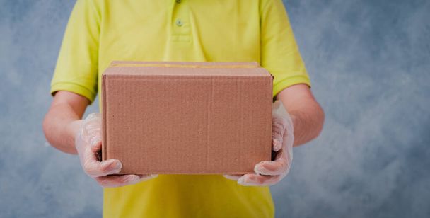 El mensajero sostiene cajas de cartón en guantes desechables. Entrega sin contacto durante el período de cuarentena del coronavirus
. - Foto, imagen
