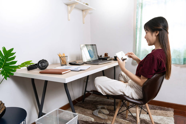 Vonzó fiatal gyönyörű ázsiai nő dolgozik laptop és dokumentum, miközben ül a beltéri nappali iroda, mint egy szabadúszó, e-coaching munka, távolról, vagy a munka otthonról koncepció - Fotó, kép