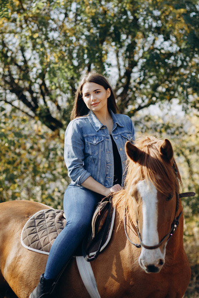 Портрет молодої жінки зі своїм конем у заміському клубі. Стиль ранчо. Дівчина дивиться в камеру
 - Фото, зображення