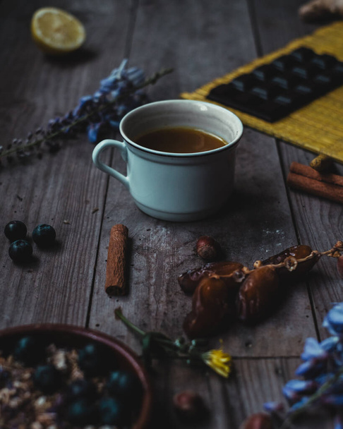 Moody turmeric cup of tea in a wood table with flowers, chocolate, nuts, blueberries, cinnamon, dates - Photo, Image