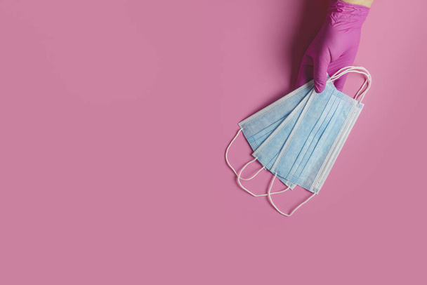 El médico sostiene la mascarilla quirúrgica respiratoria en las manos guantes médicos de color rosa sobre fondo rosa. Virus de la corona pandémica, seguro, enfermedades transmitidas por el aire, SARS, grippe
.  - Foto, imagen