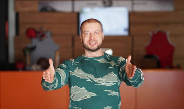 Усміхнений чоловік середнього віку в зеленому светрі показує своїми руками розмір предмета
 - Фото, зображення