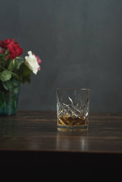 Glass of whiskey and roses on a wooden table. - Fotoğraf, Görsel