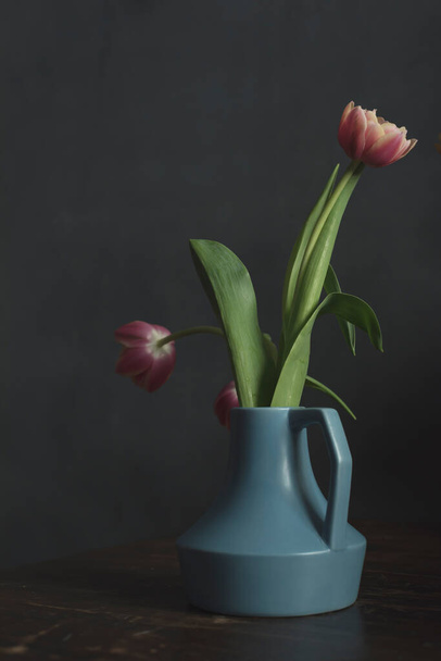木のテーブルの上にピンクのチューリップと青のヴィンテージ花瓶. - 写真・画像