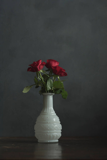 Drie rode rozen in witte antieke vaas op houten tafel. - Foto, afbeelding