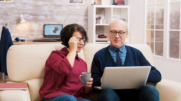 Dziadkowie w okularach siedzą na kanapie i rozmawiają z rodziną - Zdjęcie, obraz