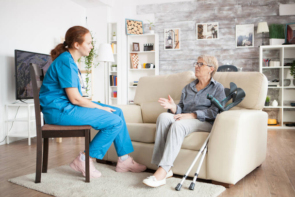 Verpleegster op een stoel in een verpleeghuis praten met oudere leeftijd vrouw - Foto, afbeelding
