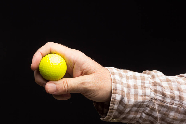 Żółta piłka golfowa na czarnym tle, w ręku osoby dorosłej. - Zdjęcie, obraz