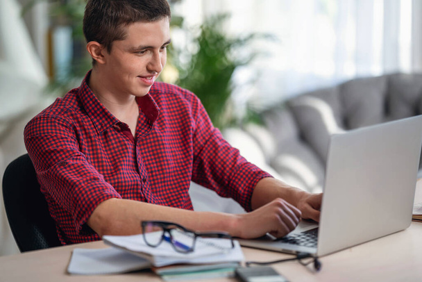 Active teen guy watching training video. does homework using laptop, writes in notebook. concept of online learning. Chat with your friends online. Social distance, self-isolation. Distance learning. - Photo, Image