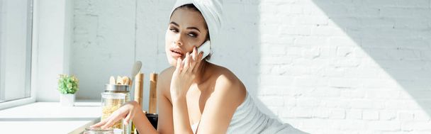 Panoramic shot of sensual woman in towels talking on smartphone in kitchen  - Foto, imagen