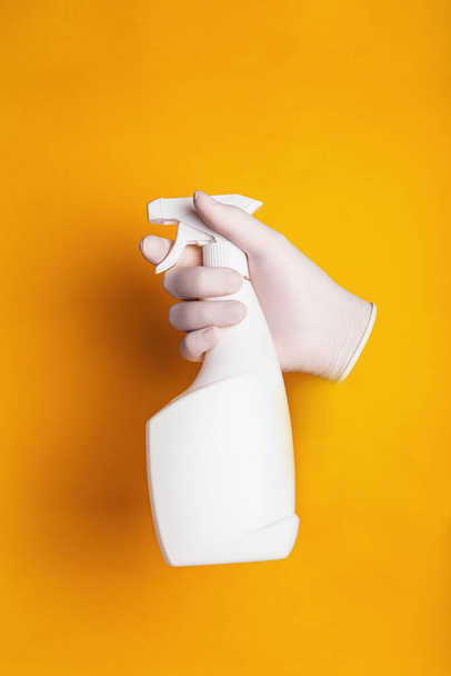A male hand in a medical glove holds a spray bottle on a yellow background - Zdjęcie, obraz