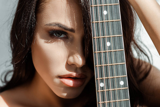 Όμορφη γυναίκα κοιτάζει κάμερα κρατώντας ακουστική κιθάρα  - Φωτογραφία, εικόνα
