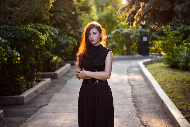 Beautiful, young woman in a black dress with a corset walking in the park in the evening at sunset. - Foto, immagini