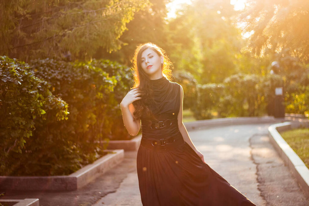 Beautiful, young woman in a black dress with a corset walking in the park in the evening at sunset. - Photo, Image
