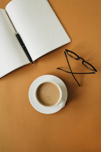 Moderner Schreibtisch im Home Office mit Notizbuch, Tasse Kaffee, Gläser auf Ingwer-Hintergrund. Arbeit, Geschäftskonzept. - Foto, Bild