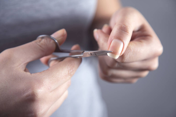 woman cut the nail with scissors on grey background - Valokuva, kuva