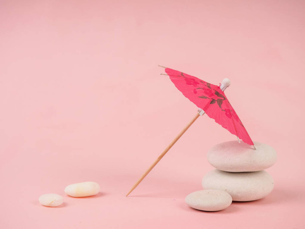 Cocktail umbrella. Pink paper cocktail umbrella isolated on pink. paper pink umbrella on pink stones, near white stones, the concept of leisure and minimalism. - Photo, Image