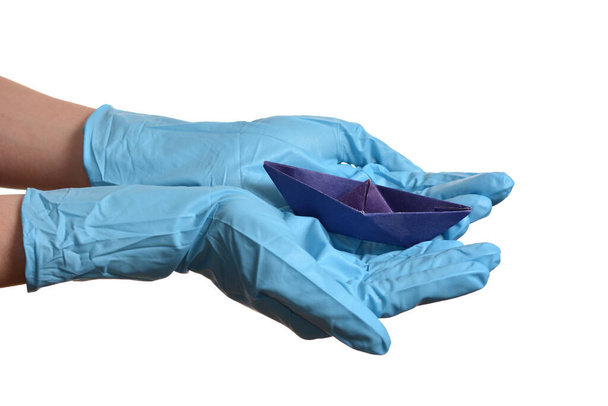 Origami papieren boot in de hand met rubberen handschoenen over wit - Foto, afbeelding
