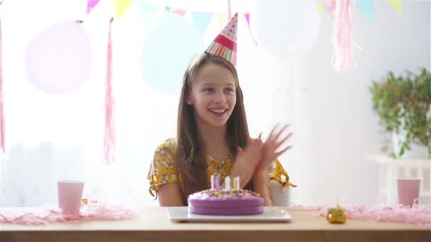 白人の女の子は夢のように笑って誕生日の虹のケーキを見ています。風船で祭りのカラフルな背景。誕生会と願いのコンセプト. - 映像、動画