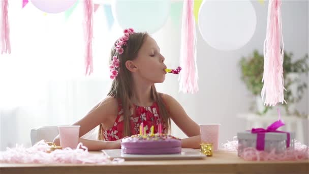 Caucasian girl is dreamily smiling and looking at birthday rainbow cake. Festive colorful background with balloons. Birthday party and wishes concept. - Footage, Video