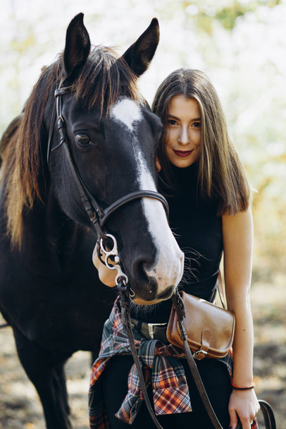 Portrait of young woman with her horse in country club. Ranch style. Girl looking in camera - Photo, Image