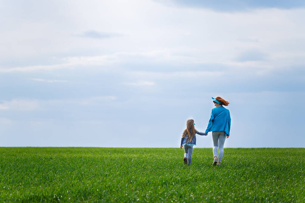 Kind und Mutter rennen und springen, grünes Gras auf dem Feld, sonniges Frühlingswetter, Lächeln und Freude des Kindes, blauer Himmel mit Wolken - Foto, Bild