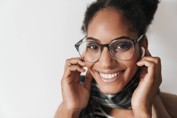 Portrait closeup of african american joyful woman in eyeglasses laughing and using earpods isolated over white background - Foto, imagen