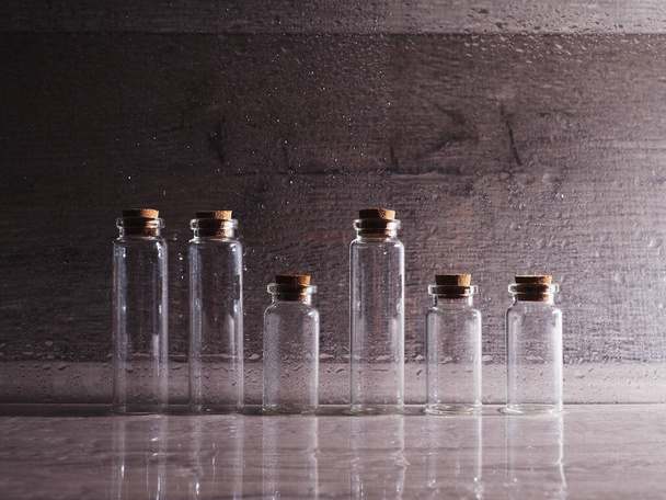 Pequeñas botellas de vidrio con tapa de corcho. burbujas vacías en luz contorneada sobre fondo de madera, gran pancarta, espacio para el diseño
. - Foto, imagen