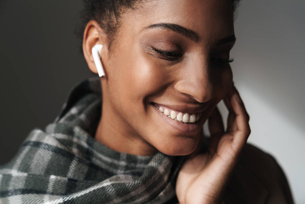 Portrait of african american attractive woman smiling and using earpod isolated over grey background - Fotografie, Obrázek