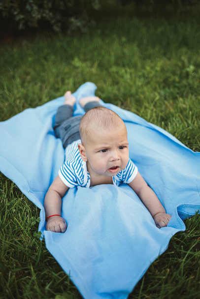 Il bambino di 3 mesi giace sul suo stomaco su un copriletto blu nel parco intorno all'erba verde e agli alberi. Emozioni da bambini di gioia
 - Foto, immagini