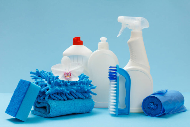 Plastic bottles of dishwashing liquid, glass and tile cleaner, garbage bags, rags, a brush and a sponge on the blue background. Washing and cleaning set. - Photo, Image