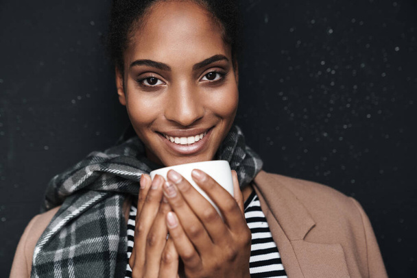 Portrait closeup of african american attractive woman smiling and drinking coffee isolated over black wall - Fotoğraf, Görsel
