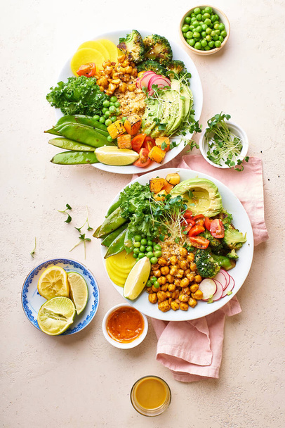 Healthy vegetarian lunch bowls with avocado and chickpeas with quinoa and vegetables garnished with microgreens and nut dressing  on stone background - Photo, image