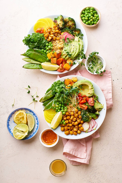 Healthy vegetarian lunch bowls with avocado and chickpeas with quinoa and vegetables garnished with microgreens and nut dressing  on stone background - Foto, Imagem