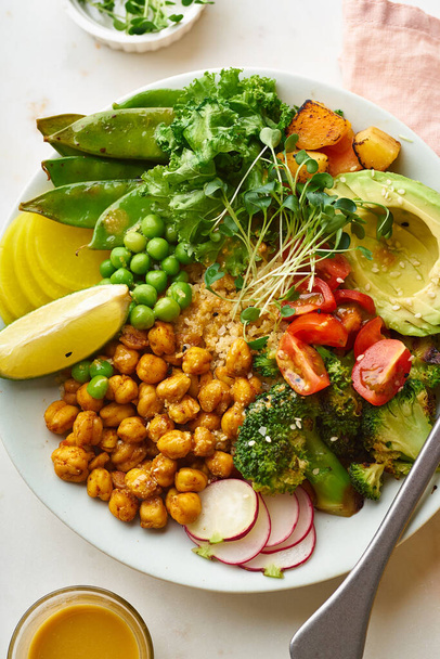 Healthy vegetarian lunch bowl with avocado and chickpeas with quinoa and vegetables garnished with microgreens and nut dressing  on stone background - Foto, imagen