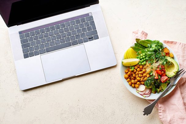 laptop and healthy vegetarian lunch bowl with avocado and chickpeas with quinoa and vegetables garnished with microgreens and nut dressing. Good food for work concept.  - Foto, Bild