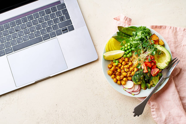 laptop and healthy vegetarian lunch bowl with avocado and chickpeas with quinoa and vegetables garnished with microgreens and nut dressing. Good food for work concept.  - Фото, изображение