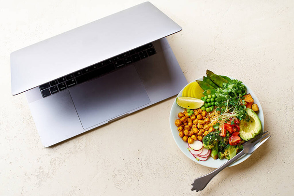 laptop and healthy vegetarian lunch bowl with avocado and chickpeas with quinoa and vegetables garnished with microgreens and nut dressing. Good food for work concept.  - Photo, Image